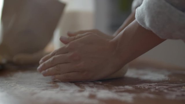 Close up of female baker hands making dough for bread on wooden table