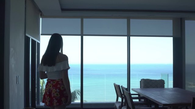 Wide shot of women closing automatic blinds with beautiful blue ocean view in background