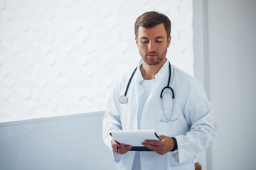 Portrait of confident male doctor with stethoscope and documents that stands in the clinic