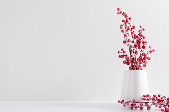 Winter composition of white branches, red berries and leaves with sparkles in vase on white background. Christmas, New Year, winter concept. Front view, copy space