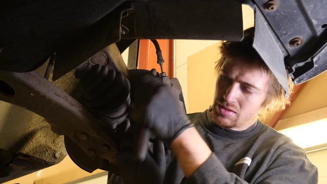 Expert mechanic using a socket wrench to tighten the bolt holding the caliper in place after repairing the car's disc break system