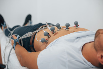 Man lying on the bed in the clinic and getting electrocardiogram test - obrazy, fototapety, plakaty