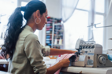 Dressmaker woman sews clothes on sewing machine in factory