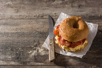 Bagel sandwich with slab bacon, egg and cheese on wooden table. Copy space