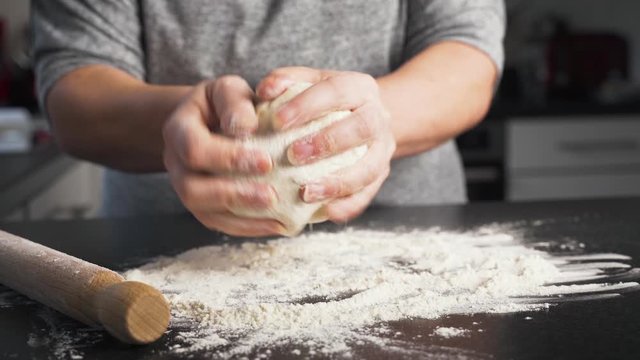 Woman rolling a ball of dough in flour on a black kitchen counter and wooden rolling pin. Pastry chef working with her hands to knead dough getting ready to bake a dessert.
