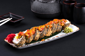 Top view close up of assorted spicy sushi set with salmon, shrimp, caviar, mussels, tuna, cream cheese and hot sauce and chopsticks, soy on black background. Japanese sashimi raw food menu.