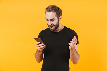 Image of excited man wearing t-shirt smiling and holding smartphone