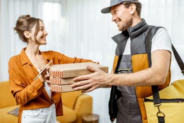 Handsome courier in uniform delivering pizza with thermal bag to a client home, happy woman...
