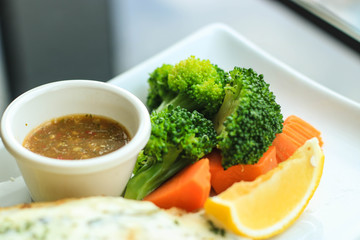 Closed up broccoli, carrot and lemon served with seafood sauce on white plate