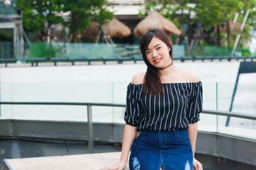 Young woman wears black off shoulder top and jeans skirt posing and smiling on rooftop's department store in Bangkok, Thailand. Woman feels happy when she travels on holiday.