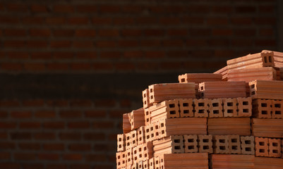 Pile of red clay building bricks on red brick wall background in construction area