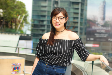 Asian beautiful girl wears black off shoulder top and jeans skirt posing on rooftop with urban landscape in Bangkok, Thailand
