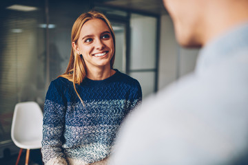 Young blonde woman smiling while answering questions during interview for getting job offer in office,happy female communicating with colleague during work break enjoying friendly atmosphere - obrazy, fototapety, plakaty