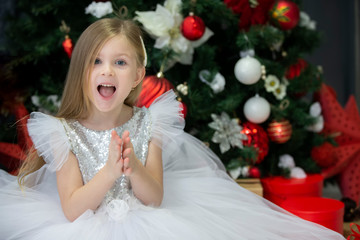 Beautiful child with a christmas gift. Dressing up girl at the New Year tree.