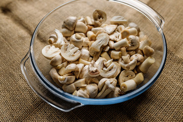 Cut forest champignon mushrooms in glass bowl standing on table covered with sackcloth.