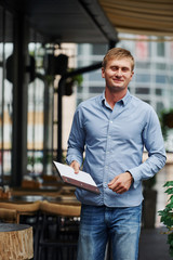 Front view of guy in jeans that stands in the cafe at daytime