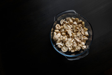 Cut forest champignon mushrooms in glass bowl on dark background or black wooden table.