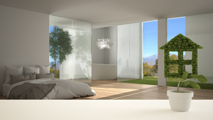 White table top or shelf with green plant in pot shaped like house, modern bedroom with inner garden in the background, interior design, real estate, eco architecture concept idea
