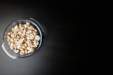Cut forest champignon mushrooms in glass bowl on dark background or black wooden table.