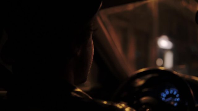 Stylish Man in hat driving a Car in Paris at Night, with brurred night street lights