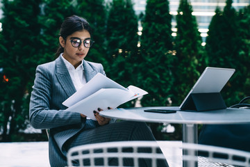 Professional economist using paper documents and portable pc for checking monthly report, Latino...