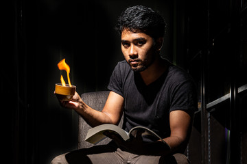 Portrait of Asian black man wear solid black shirt and green plant make serious face looking straight holding book and cup of fire in hand isolate in dark background stock photo