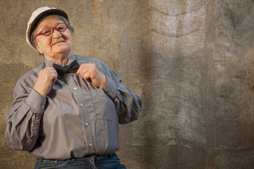 Extravagant old woman with gray hair and wrinkles in glasses. pensioner adjusts a bow tie. concept of domineering and funny elderly mother-in-law. Humor in studio