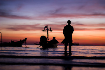 silhouette man standing alone seeing the beautiful colorful twilight sunset sky with orange pink purple at the seascape background.many fishing long tail boat chill and calm emotion cold mood & tone.