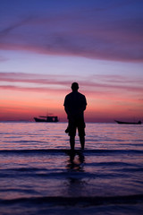 silhouette man standing alone seeing the beautiful colorful twilight sunset sky with orange pink purple at the seascape background.many fishing long tail boat chill and calm emotion cold mood & tone.