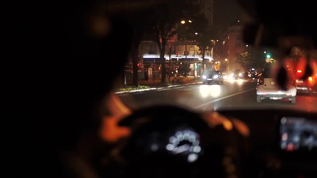 Stylish Man in hat driving a Car in Paris at Night, with brurred night street lights