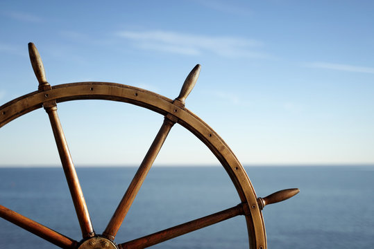 Ship wheel and blue sea on background.