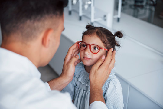 Young Pediatrician In White Coat Helps To Get New Glasses For Little Girl