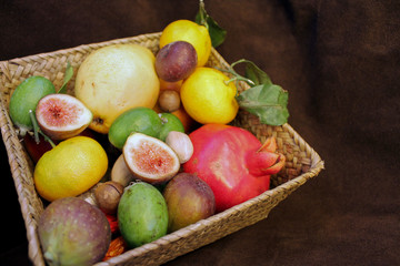 autumn fruit harvest in a basket on a dark brown suede background. pomegranate, Fig, feijoa, Mandarin, pear, Brazil nut. horizontal, copy space, front view