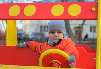 Fototapeta na wymiar cute little boy sitting behind the wheel of a baby car in the Playground
