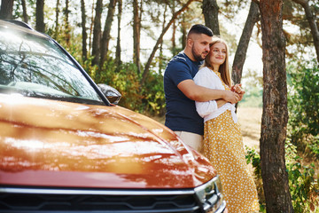 Couple embracing each other in the forest near modern car