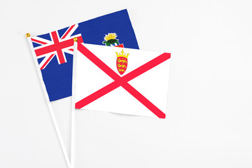 Fototapeta na wymiar Jersey and Cayman Islands stick flags on white background. High quality fabric, miniature national flag. Peaceful global concept.White floor for copy space.