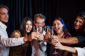 Knocking glasses. Group of friends in festive clothes have party indoors together