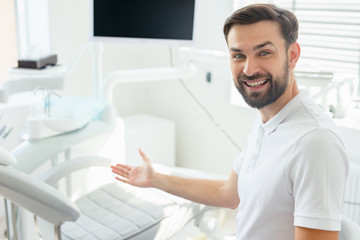 Smiling doctor sitting with folded arms in modern dental clinic