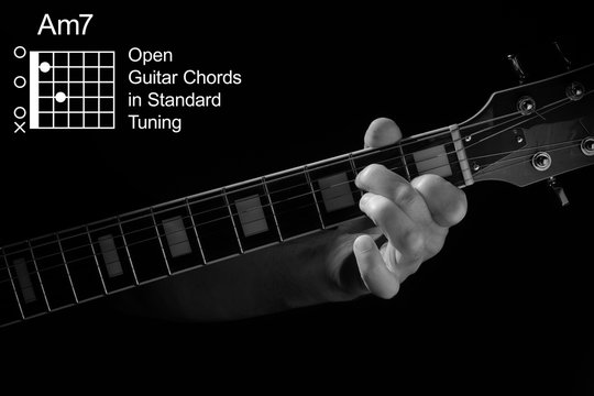 Open Guitar Chords in Standard Tuning guitar tutorial series. Closeup of hand playing Am7 chord on guitar, on black background. Black and white photo.