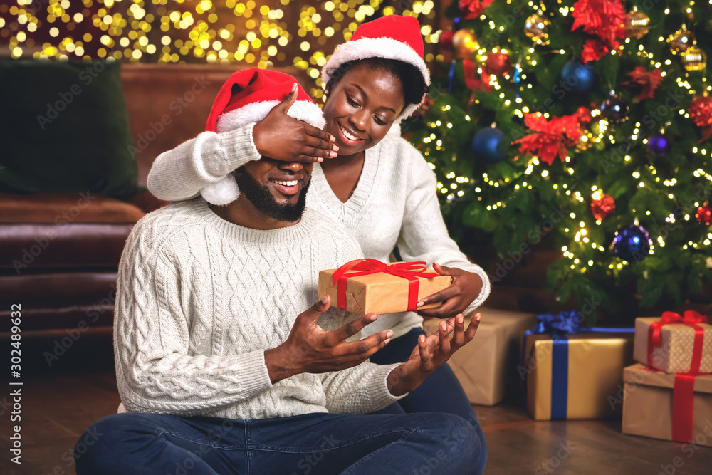 Wall mural Black girl closing eyes to boyfriend while giving him present