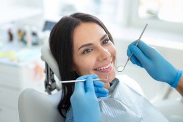 male dentist examining teeth of attractive smiling client