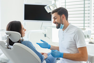 side view of dentist advicing and gesturing to patient in modern clinic