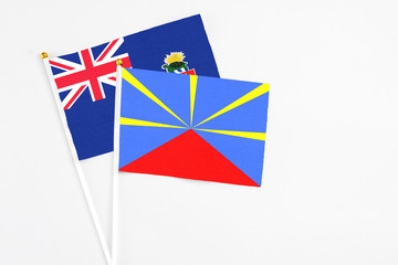Fototapeta premium Reunion and Cayman Islands stick flags on white background. High quality fabric, miniature national flag. Peaceful global concept.White floor for copy space.