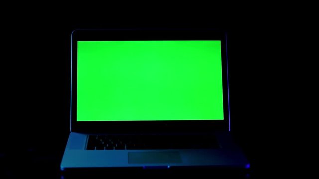 Laptop with green screen in neon light on black backgound Dark Office.