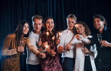 Having fun with sparklers. Group of cheerful friends celebrating new year indoors with drinks in hands