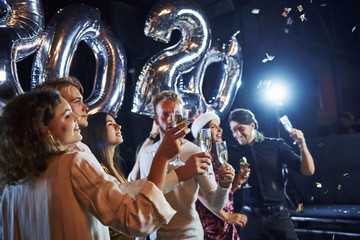 Fototapeta na wymiar Cheerful group of people with drinks and balloons in hands celebrating new 2020 year