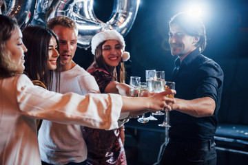 Group of cheerful friends celebrating new year indoors with drinks in hands