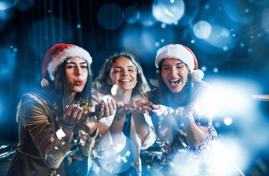 Three Women Blowing Confetti From Their Hands Indoors At Holiday Time