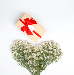 Gift box with red ribbon on above of heart shape created from white cutter flower on white wooden background. Top view. Gift time. Valentine day concept.