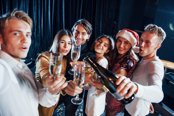 Takes selfie. Group of cheerful friends celebrating new year indoors with drinks in hands